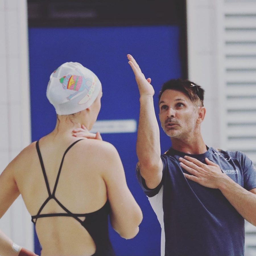 An AIS coach working with a swimmer at the pool deck